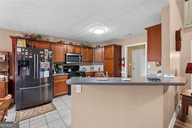 kitchen with visible vents, brown cabinets, a peninsula, stainless steel appliances, and light tile patterned flooring