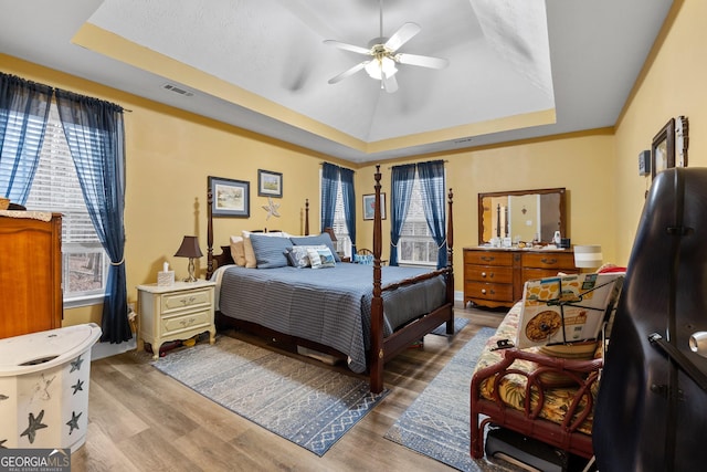 bedroom featuring ceiling fan, light wood-type flooring, a raised ceiling, and visible vents