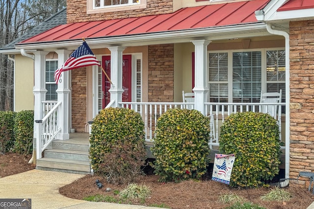 view of exterior entry with a standing seam roof, metal roof, a porch, and brick siding