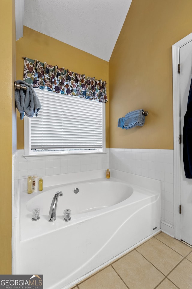 full bath with vaulted ceiling, a bath, and tile patterned floors