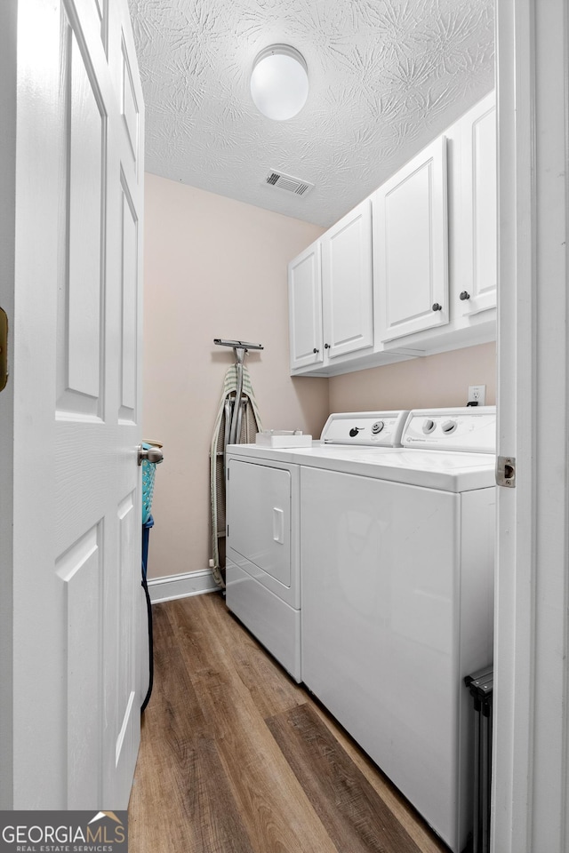 clothes washing area with washer and clothes dryer, visible vents, cabinet space, a textured ceiling, and wood finished floors