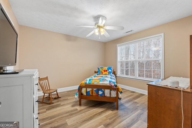 bedroom featuring visible vents, light wood-style flooring, ceiling fan, a textured ceiling, and baseboards