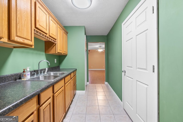 kitchen with dark countertops, ceiling fan, a textured ceiling, a sink, and light tile patterned flooring