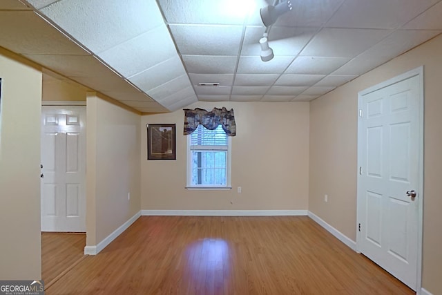 interior space with baseboards, a drop ceiling, and wood finished floors