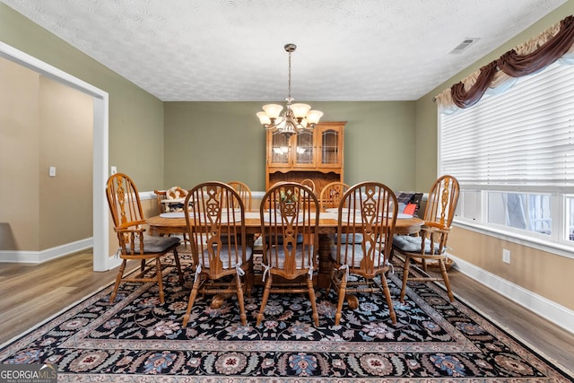 dining space with a chandelier, wood finished floors, visible vents, and baseboards