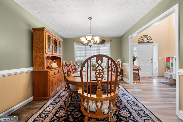 dining space featuring a textured ceiling, light wood finished floors, baseboards, and an inviting chandelier