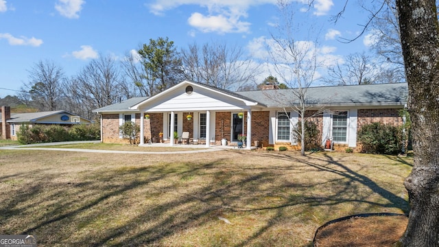 view of front facade featuring a porch, brick siding, a chimney, and a front yard