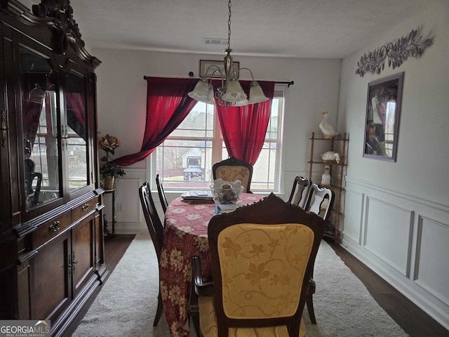 dining space featuring visible vents, a wainscoted wall, dark wood-style floors, an inviting chandelier, and a decorative wall