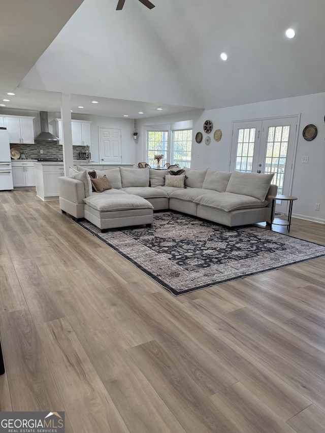 living room with baseboards, a ceiling fan, light wood-type flooring, high vaulted ceiling, and recessed lighting