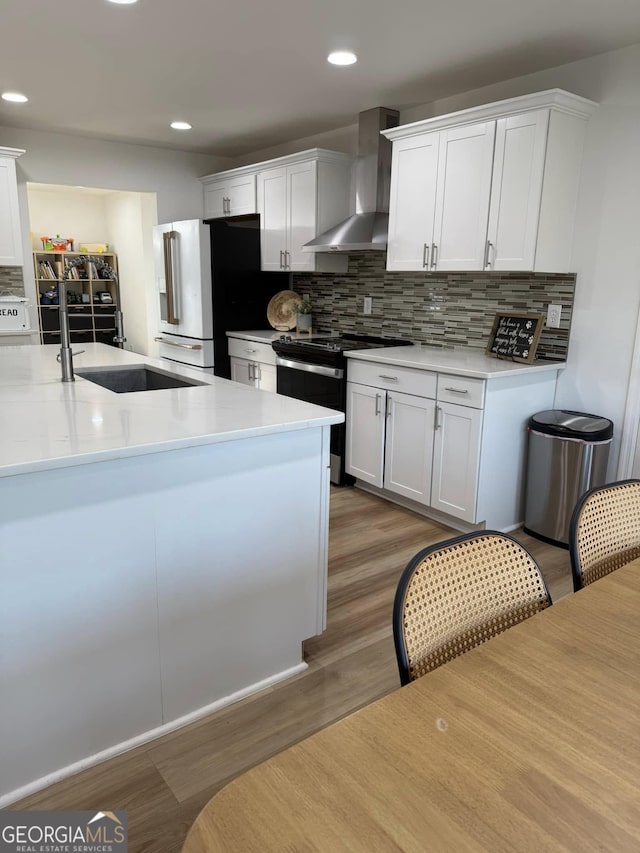 kitchen featuring a sink, high quality fridge, wall chimney range hood, wood finished floors, and black / electric stove