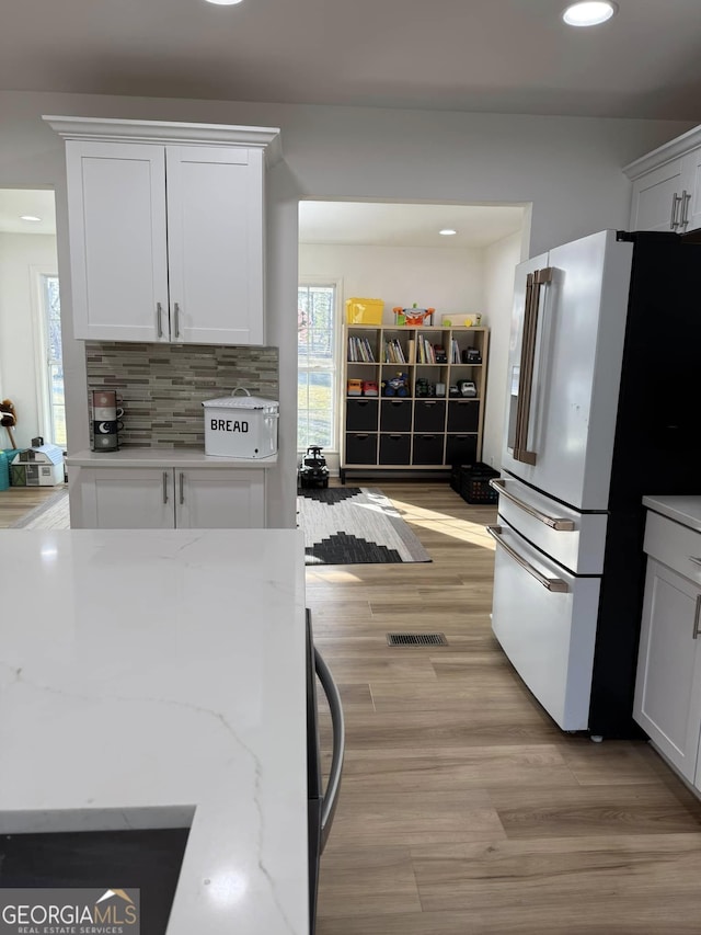 kitchen featuring light stone counters, high end white refrigerator, backsplash, light wood-style floors, and white cabinets