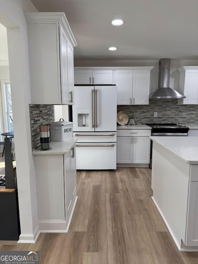 kitchen with light wood finished floors, light countertops, white cabinets, white fridge with ice dispenser, and wall chimney exhaust hood