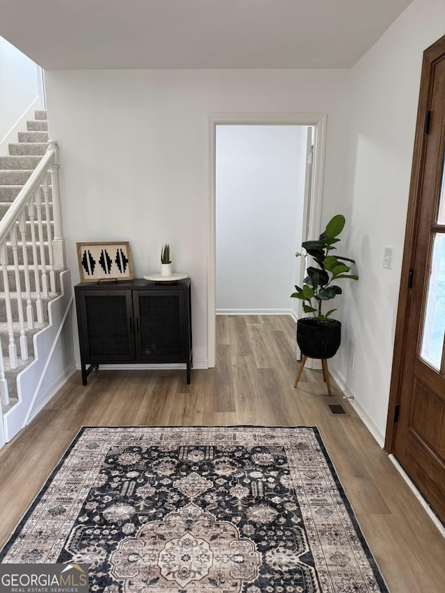 foyer featuring wood finished floors, visible vents, baseboards, and stairs