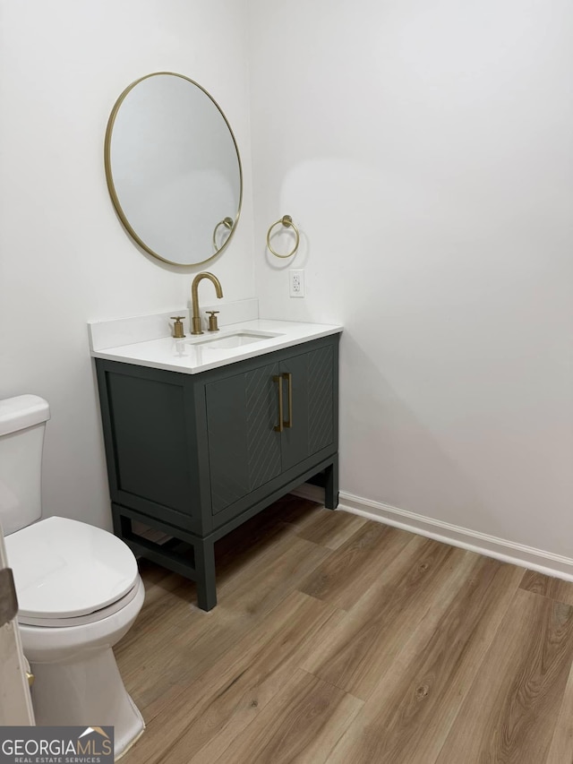 half bathroom featuring vanity, wood finished floors, toilet, and baseboards