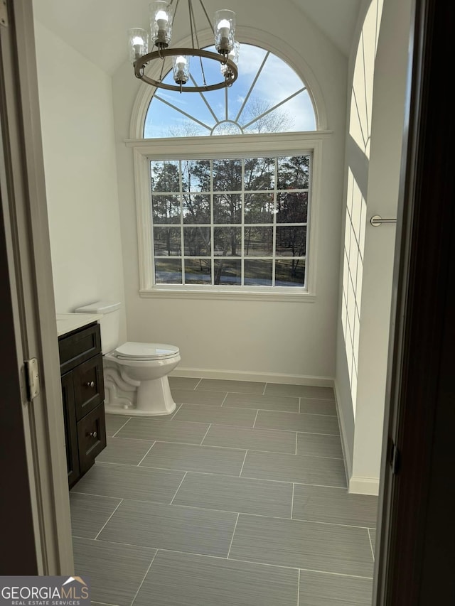 bathroom with baseboards, vanity, toilet, and a notable chandelier