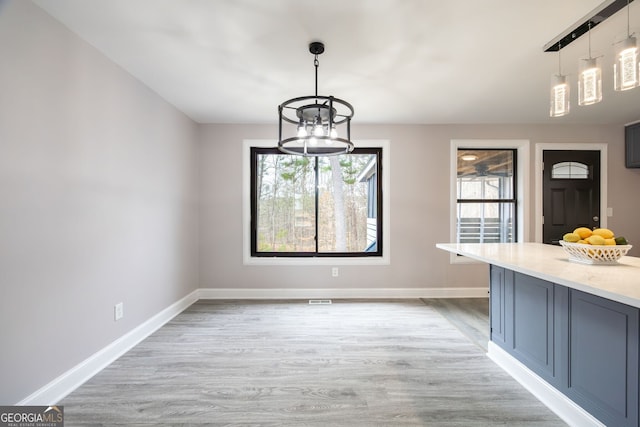 unfurnished dining area with a healthy amount of sunlight, light wood finished floors, and baseboards