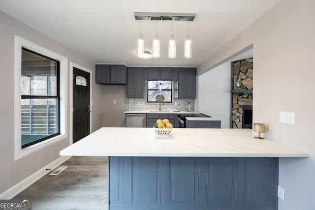 kitchen with light stone counters, backsplash, stainless steel dishwasher, a sink, and a peninsula