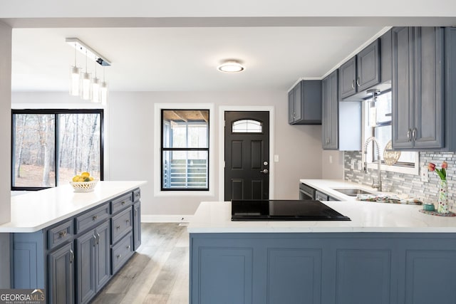 kitchen featuring light wood-style flooring, a peninsula, a sink, backsplash, and pendant lighting