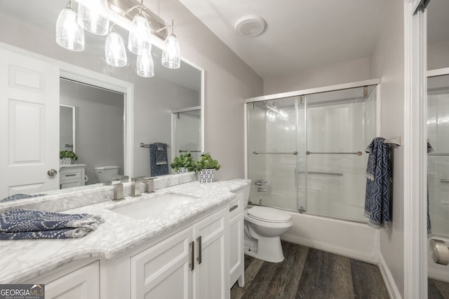 full bath with vanity, combined bath / shower with glass door, wood finished floors, and toilet