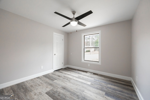 empty room with ceiling fan, wood finished floors, visible vents, and baseboards