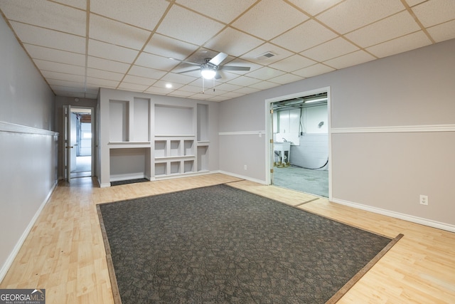 unfurnished living room featuring a ceiling fan, wood finished floors, a paneled ceiling, and baseboards