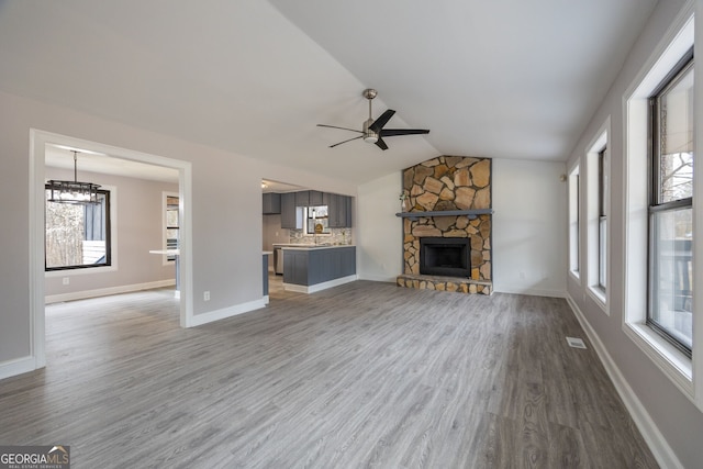 unfurnished living room with a fireplace, visible vents, vaulted ceiling, wood finished floors, and ceiling fan with notable chandelier