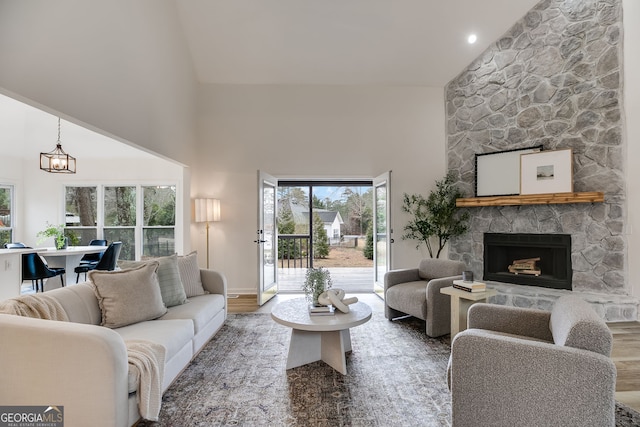 living room with a chandelier, high vaulted ceiling, a fireplace, and wood finished floors