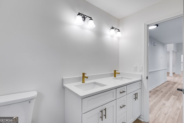 bathroom featuring double vanity, wood finished floors, a sink, and toilet