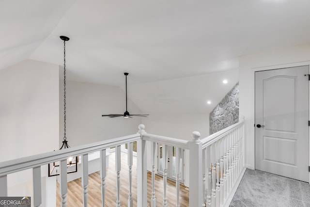 corridor with vaulted ceiling, light wood-type flooring, and an upstairs landing