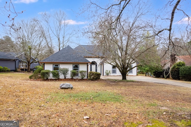 view of front facade with driveway, roof with shingles, and a front yard