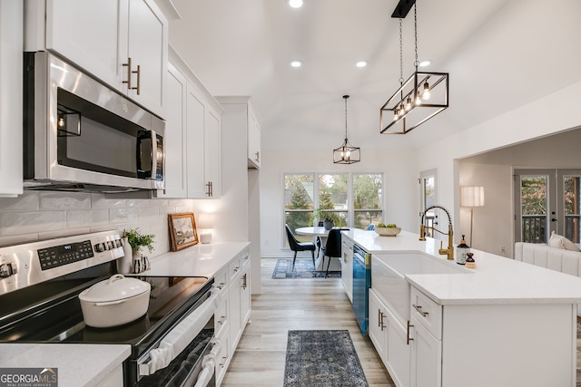 kitchen with stainless steel appliances, a sink, white cabinetry, light wood-style floors, and backsplash