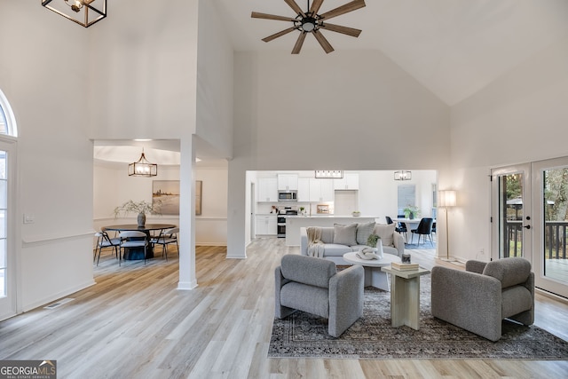 living area with high vaulted ceiling, light wood-type flooring, visible vents, and an inviting chandelier