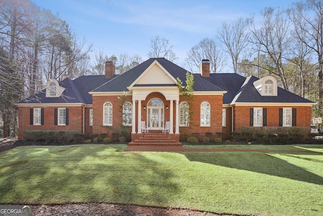 neoclassical / greek revival house with brick siding, a front lawn, and roof with shingles