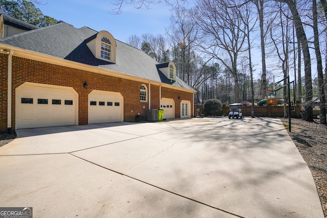 view of home's exterior featuring central AC unit, roof with shingles, an attached garage, concrete driveway, and brick siding