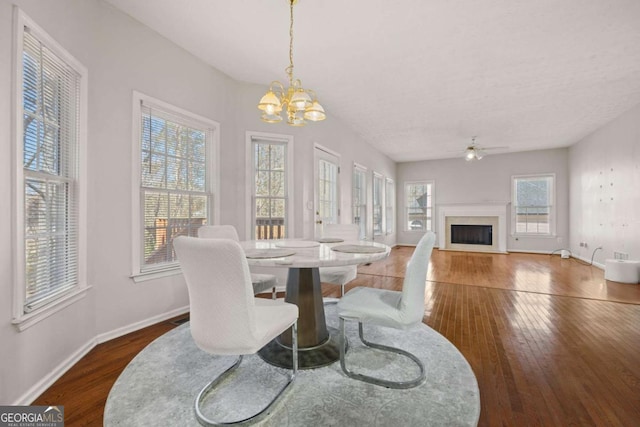 dining area featuring wood-type flooring, a fireplace, baseboards, and ceiling fan with notable chandelier