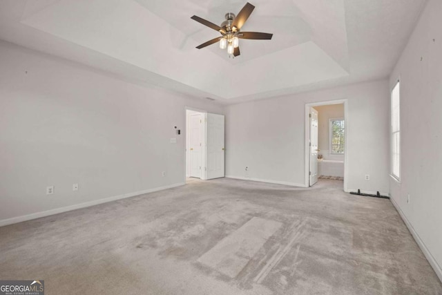carpeted empty room featuring ceiling fan, a raised ceiling, and baseboards