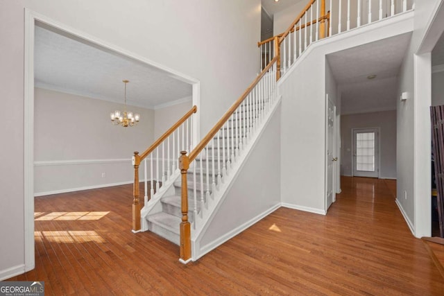 stairway featuring a towering ceiling, an inviting chandelier, baseboards, and wood finished floors