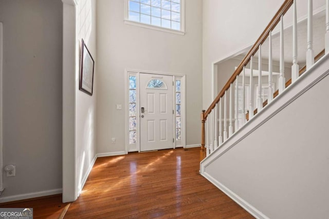entrance foyer featuring a towering ceiling, hardwood / wood-style flooring, stairway, and baseboards
