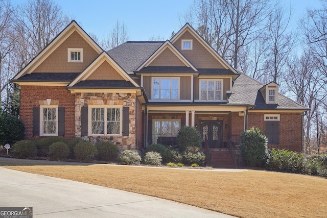 craftsman inspired home featuring brick siding, stone siding, a porch, roof with shingles, and a front lawn
