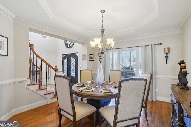 dining space featuring french doors, stairs, a chandelier, wood finished floors, and a raised ceiling