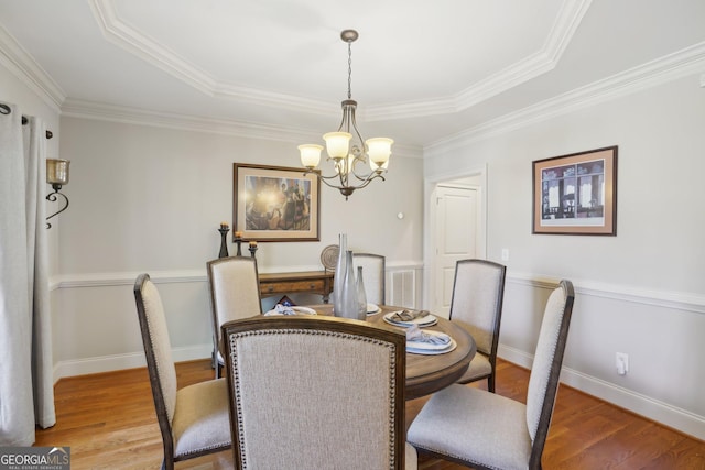 dining room featuring a raised ceiling, light wood finished floors, an inviting chandelier, and crown molding