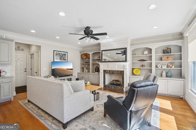 living room featuring ornamental molding, a high end fireplace, a ceiling fan, and recessed lighting