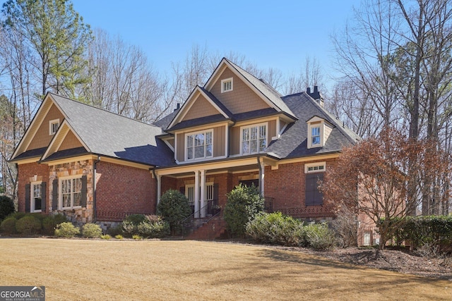 craftsman-style home with stone siding, covered porch, brick siding, and a front lawn