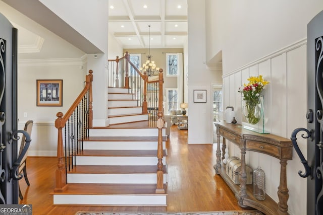 entryway with wood finished floors, stairway, coffered ceiling, a high ceiling, and a notable chandelier
