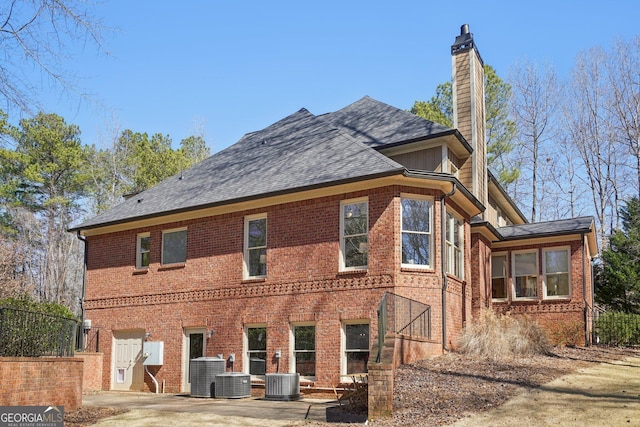 back of property with a chimney, central AC unit, and brick siding