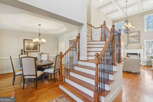 stairway with coffered ceiling, an inviting chandelier, beamed ceiling, hardwood / wood-style floors, and a fireplace