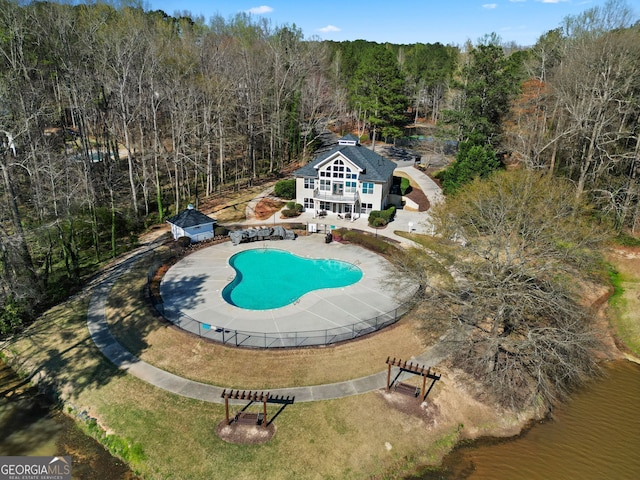 view of swimming pool featuring a patio, a fenced in pool, an outbuilding, and a view of trees