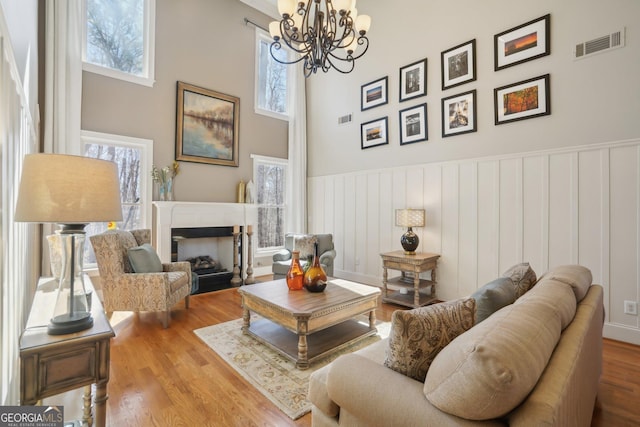 living area with wood finished floors, a wainscoted wall, a fireplace with flush hearth, visible vents, and a chandelier