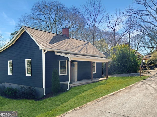 view of home's exterior with covered porch, a yard, a shingled roof, and a chimney