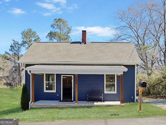 rear view of property with covered porch, a shingled roof, a chimney, and a lawn